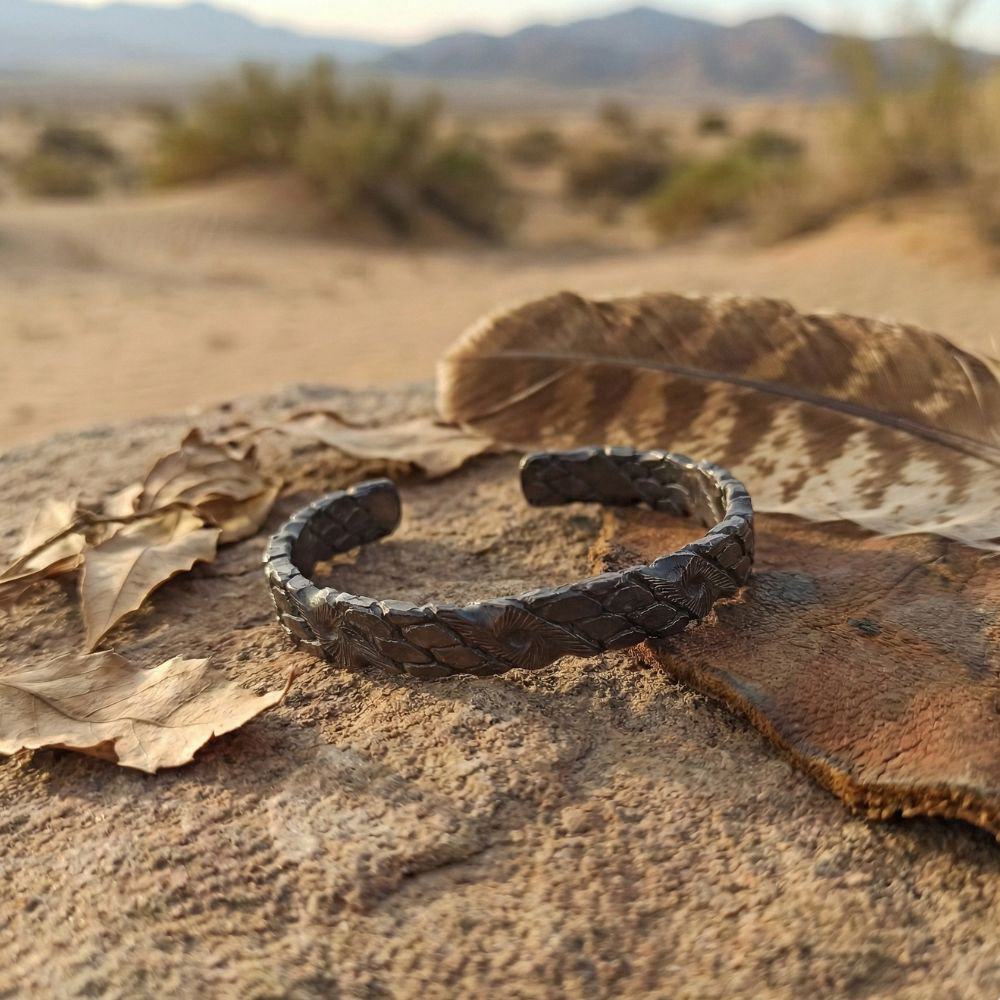 an oxidized copper twisted cuff bracelet with engraved sunburst details, shown on a rocky sandstone in an open area
