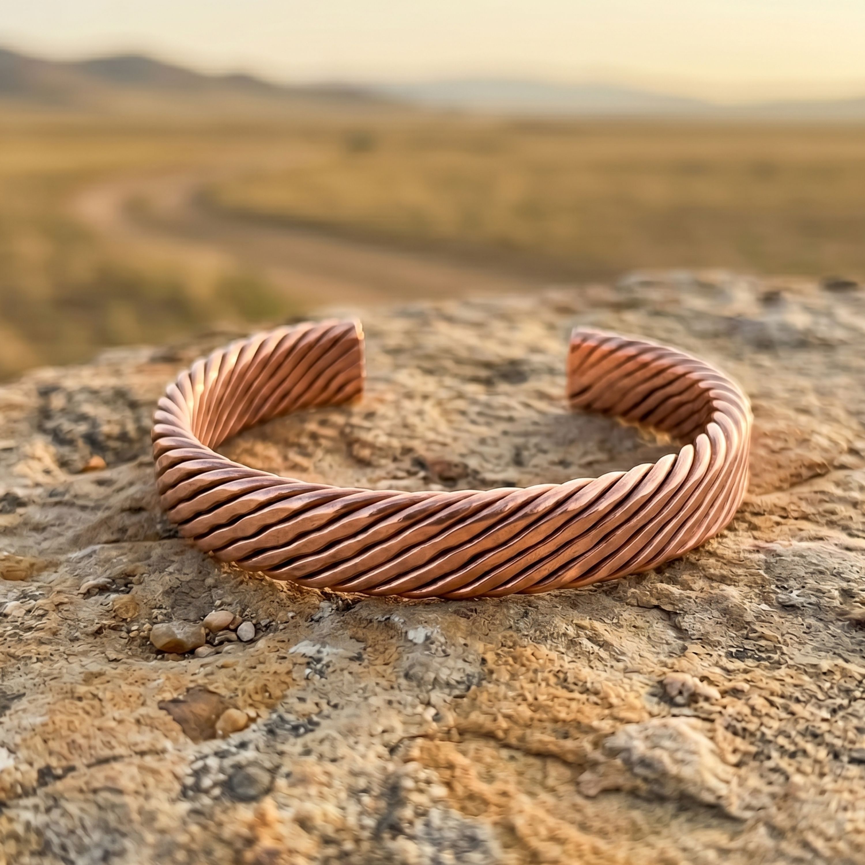 A pure copper twisted wire bracelet displayed on a rough, textured rock with a sunlit, open desert landscape in the background