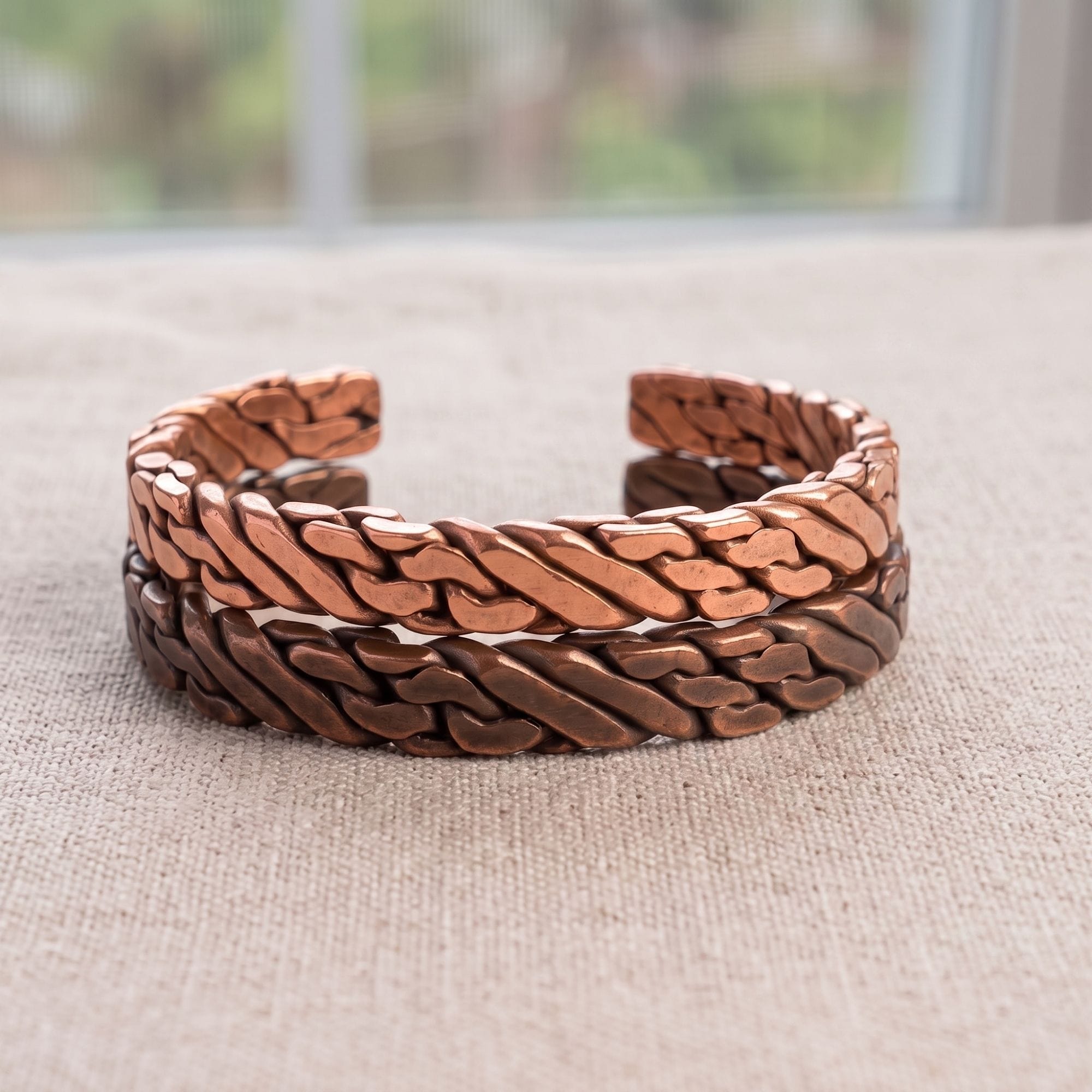 Two heavy woven men's viking bracelets stacked together on a light linen fabric. The top cuff features bright, raw solid copper, while the bottom cuff features a dark, oxidized copper finish.